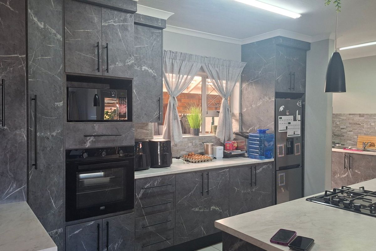 Modern kitchen featuring dark marble-effect cabinetry, stone-look countertops, built-in oven, microwave, and a central island with a gas hob.