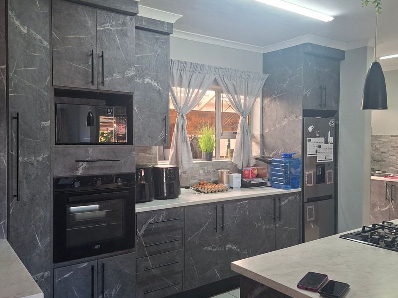 Modern kitchen featuring dark marble-effect cabinetry, stone-look countertops, built-in oven, microwave, and a central island with a gas hob.