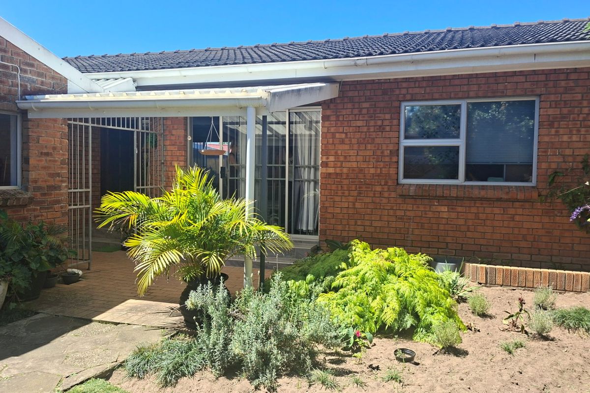 Rear exterior view of the house featuring a brick facade, tiled roof, and a covered patio area with sliding glass door access.