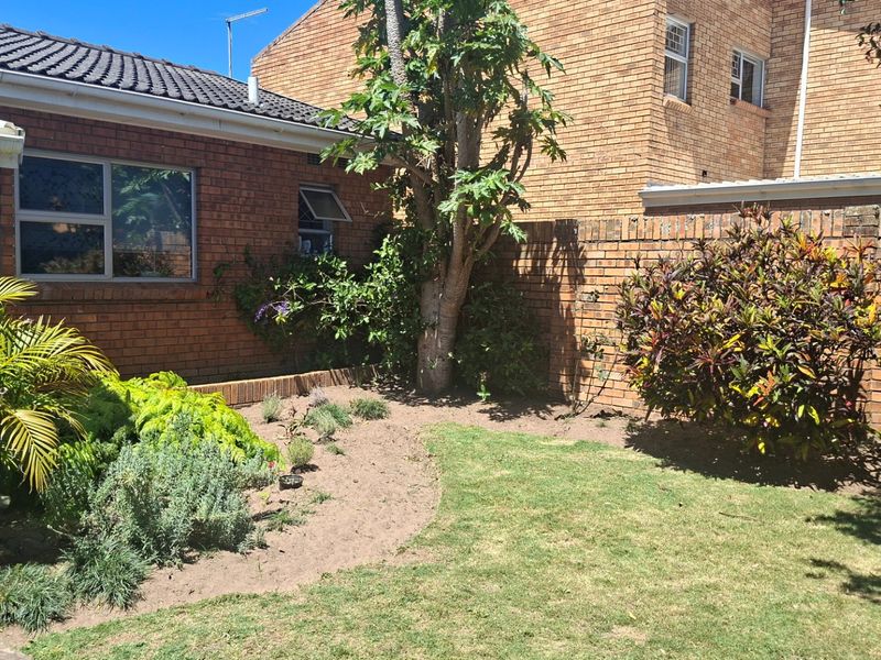A rear garden area featuring a brick boundary wall, established trees, and a lawn space adjacent to the brick-clad house exterior.