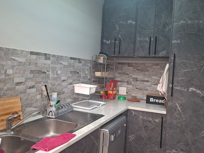 A functional scullery area featuring modern dark marble-effect cabinetry, stone-look tiled splashbacks, and a stainless steel double sink with integrated dishwasher space.