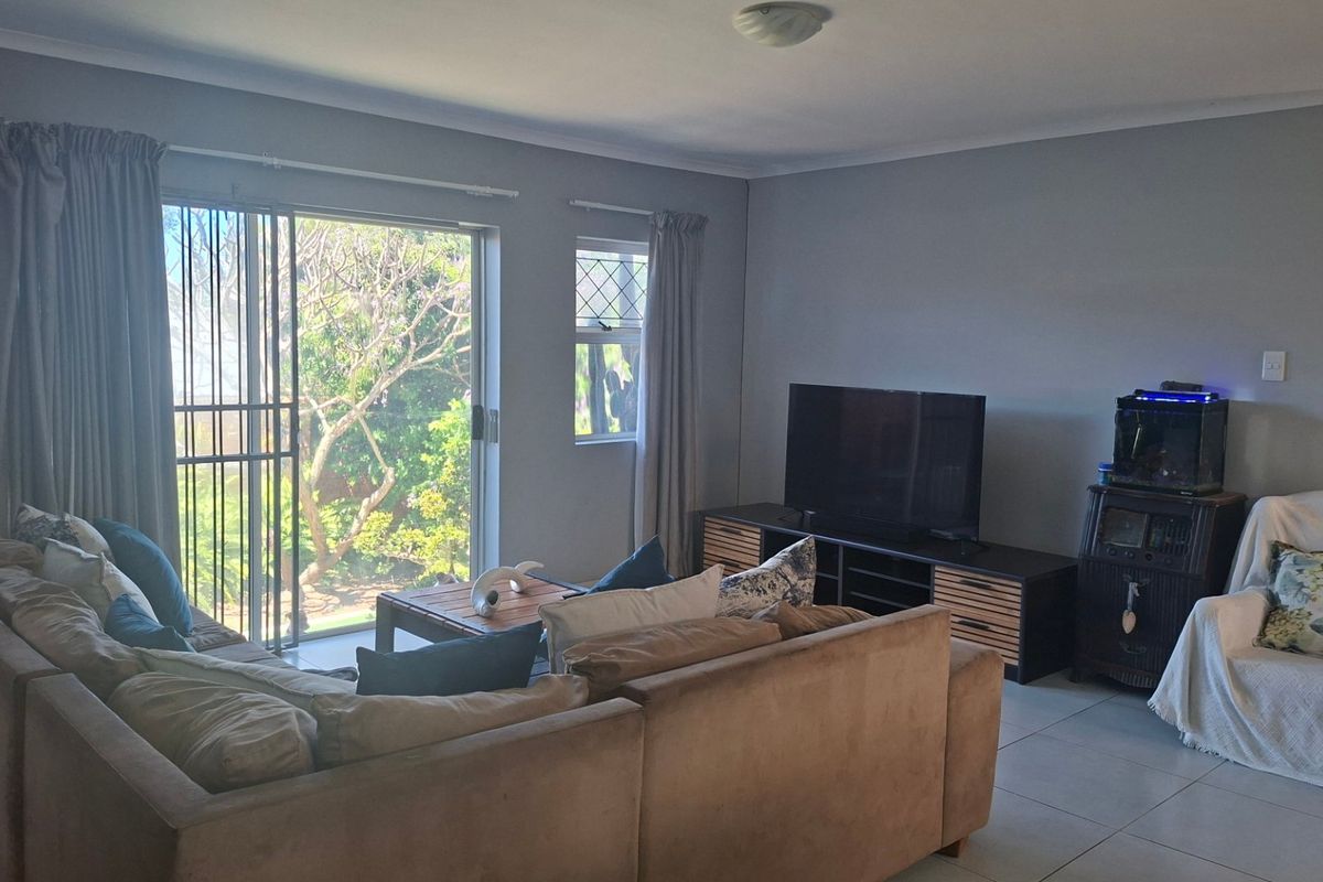 A comfortable living room featuring tiled flooring, a sliding glass door with security gate, and natural light, providing a functional space for relaxation.