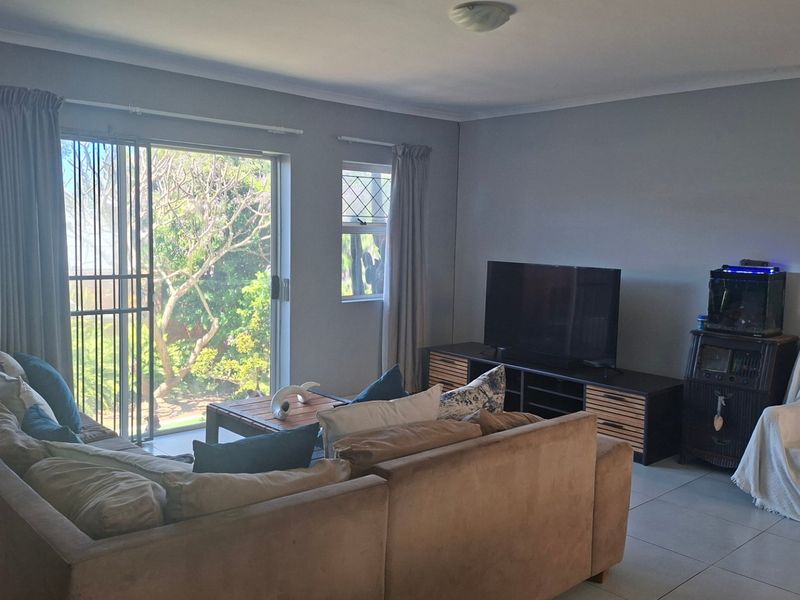 A comfortable living room featuring tiled flooring, a sliding glass door with security gate, and natural light, providing a functional space for relaxation.