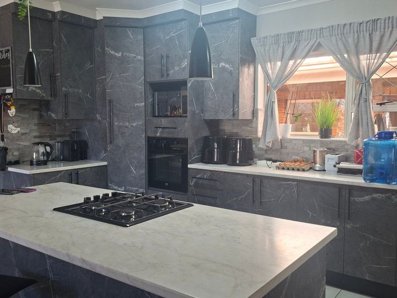 Modern kitchen featuring dark marble-effect cabinetry, a central island with a gas hob, stone tile backsplash, and integrated oven.