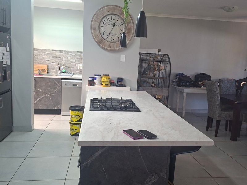 Open plan kitchen featuring a central island with a gas hob, stone countertops, and modern cabinetry, seamlessly flowing into the dining and living areas.