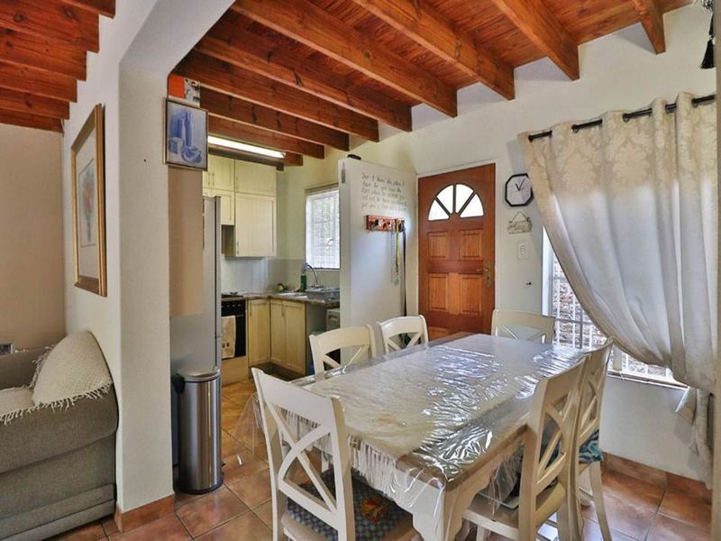 Open-plan dining and kitchen area featuring exposed timber ceiling beams, tiled flooring, and functional cabinetry with built-in cooking appliances.