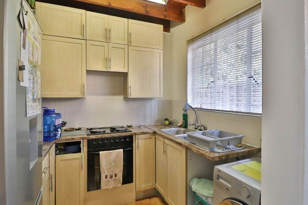 Compact kitchen featuring light-toned cabinetry, built-in oven and hob, tiled backsplash, and exposed timber ceiling beams, offering a functional layout with laundry plumbing.