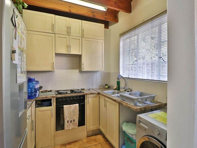 Compact kitchen featuring light-toned cabinetry, built-in oven and hob, tiled backsplash, and exposed timber ceiling beams, offering a functional layout with laundry plumbing.