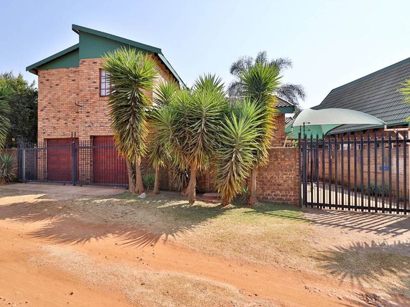 Front exterior view of a face brick townhouse featuring a double garage, secure metal gate, and a shaded parking area.