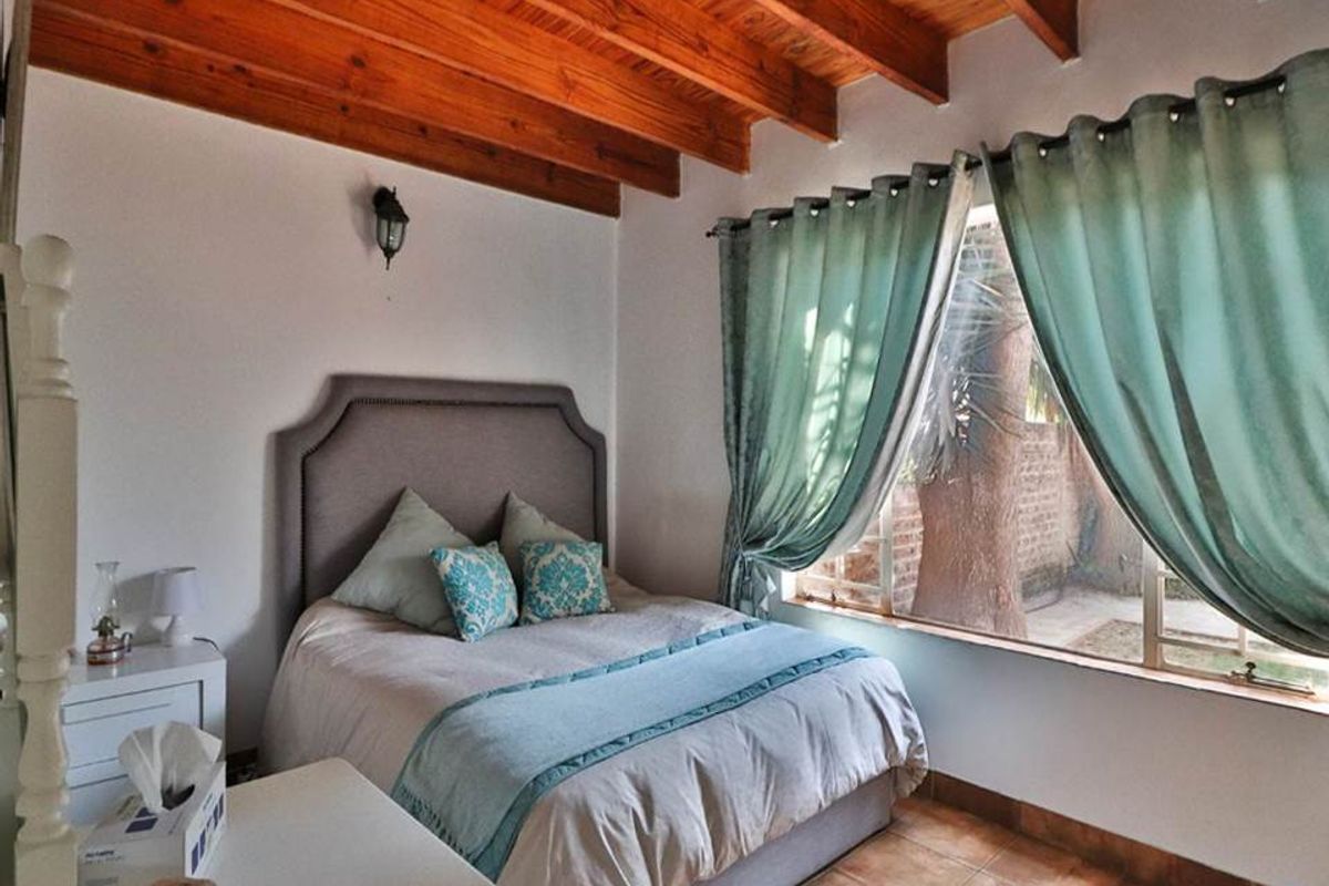 A cozy bedroom featuring exposed timber ceiling beams, tiled flooring, and a large window providing natural light and garden views.