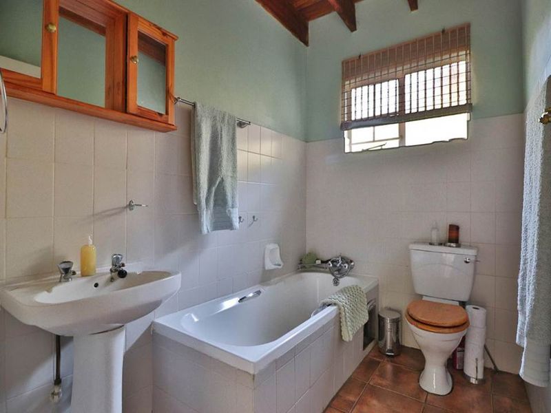 A functional bathroom featuring a pedestal basin, built-in bathtub, toilet, and classic tiled finishes with exposed timber ceiling beams.