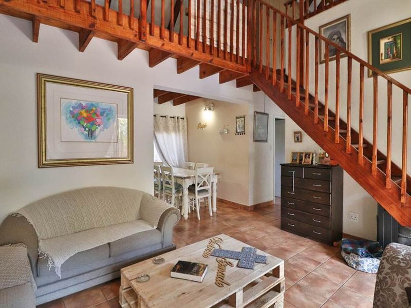 Open plan living and dining area featuring a prominent wooden staircase, exposed ceiling beams, and tiled flooring throughout.