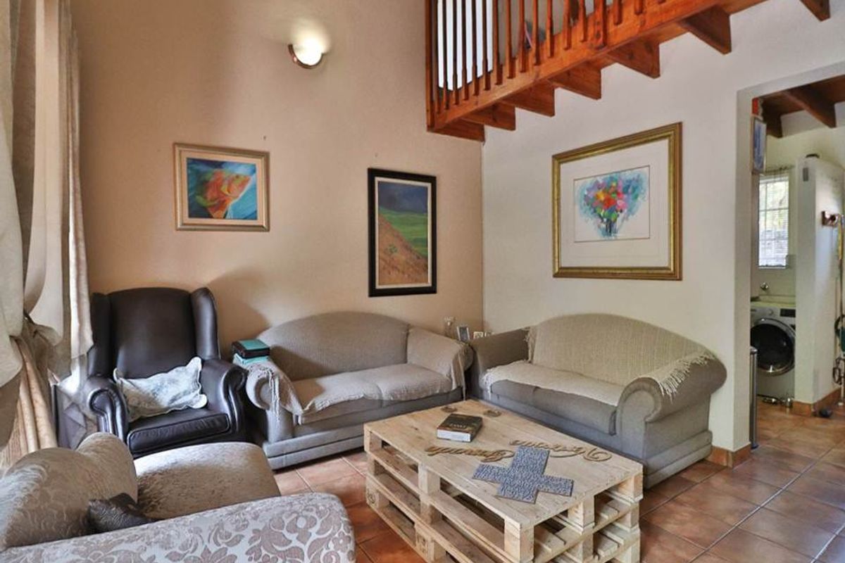A cozy living room featuring tiled flooring, a mezzanine level with a wooden staircase, and a wall sconce, offering a warm and inviting atmosphere.