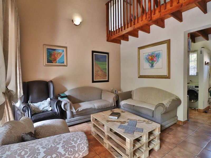 A cozy living room featuring tiled flooring, a mezzanine level with a wooden staircase, and a wall sconce, offering a warm and inviting atmosphere.