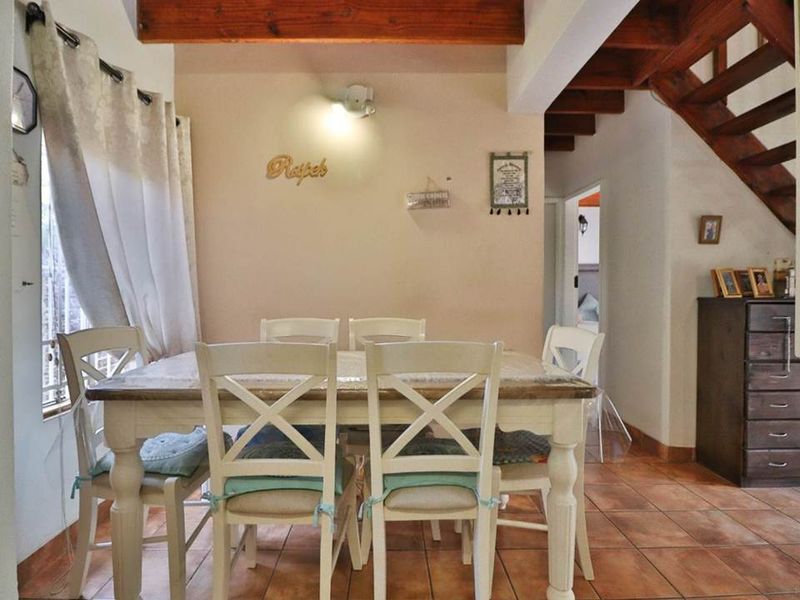 Dining area featuring exposed timber ceiling beams, a wooden staircase, and terracotta floor tiles, creating a rustic and warm atmosphere.