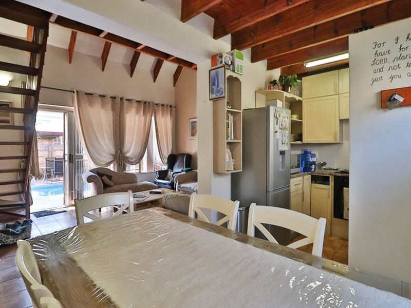 Open-plan living and dining area featuring exposed timber beams, vaulted ceilings, and a compact kitchen with direct access to an outdoor patio and pool.