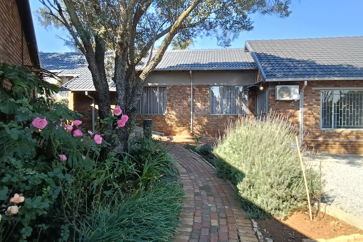 A view of the rear exterior featuring a face brick facade, tiled roof, and a brick paved pathway leading through a landscaped garden area.