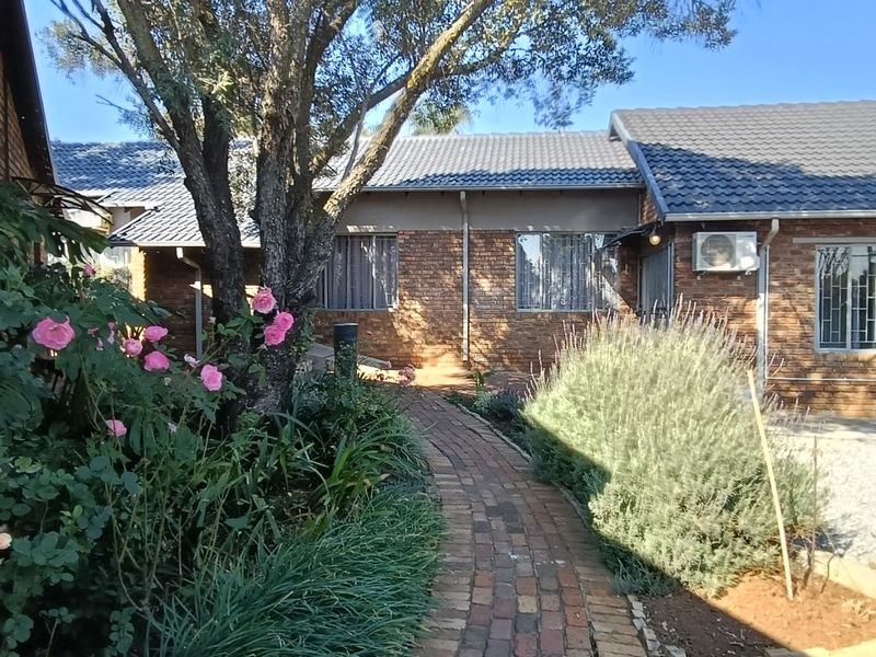 A view of the rear exterior featuring a face brick facade, tiled roof, and a brick paved pathway leading through a landscaped garden area.