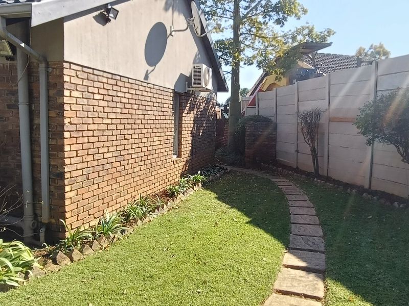 A side view of the property featuring a brick exterior wall, a manicured lawn, a stone paver pathway, and a precast concrete boundary wall.