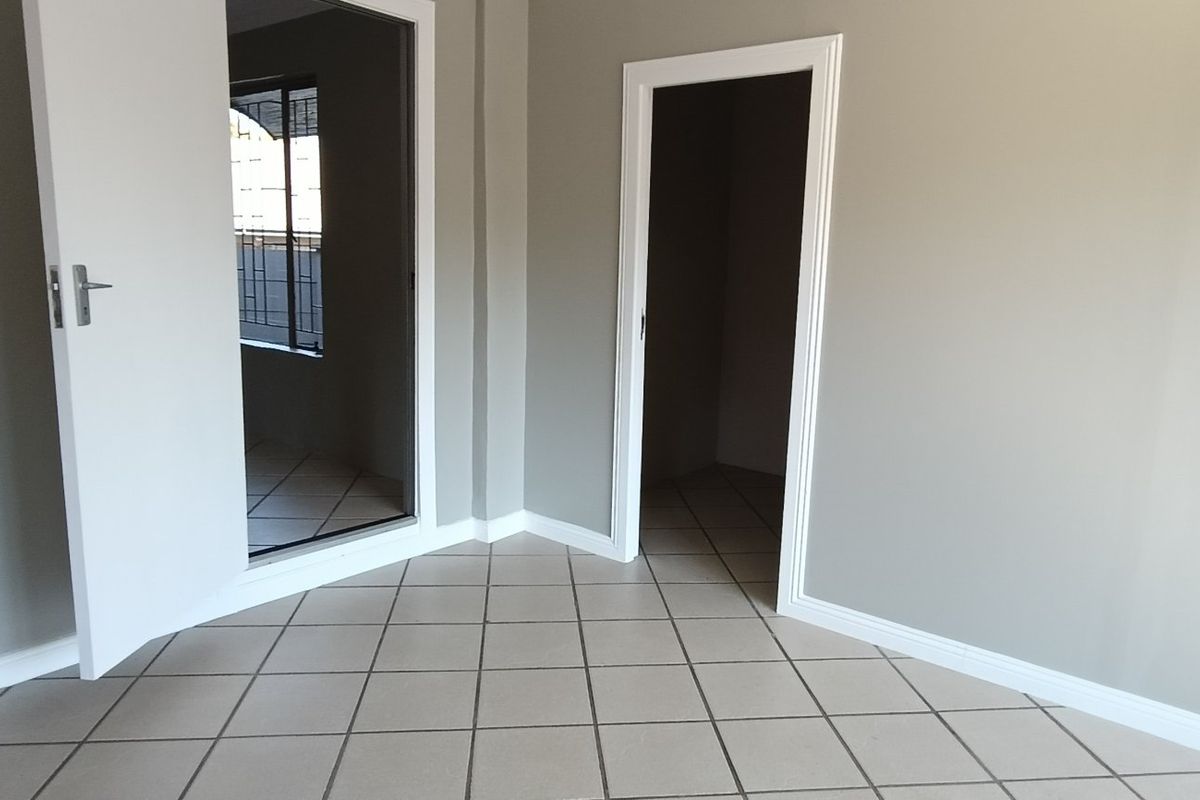 A clean, empty bedroom featuring neutral grey walls, tiled flooring, and white trim, offering a blank canvas for interior design.