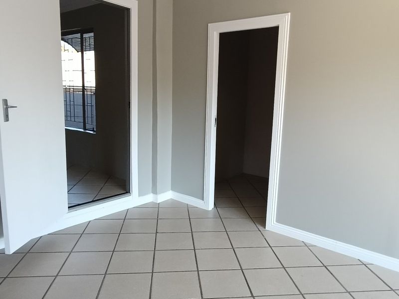 A clean, empty bedroom featuring neutral grey walls, tiled flooring, and white trim, offering a blank canvas for interior design.