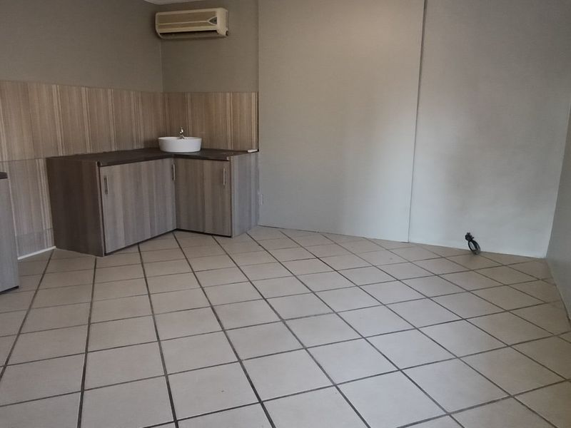 A functional, empty kitchen area featuring built-in cabinetry, a sink, tiled flooring, and a wall-mounted air conditioning unit.