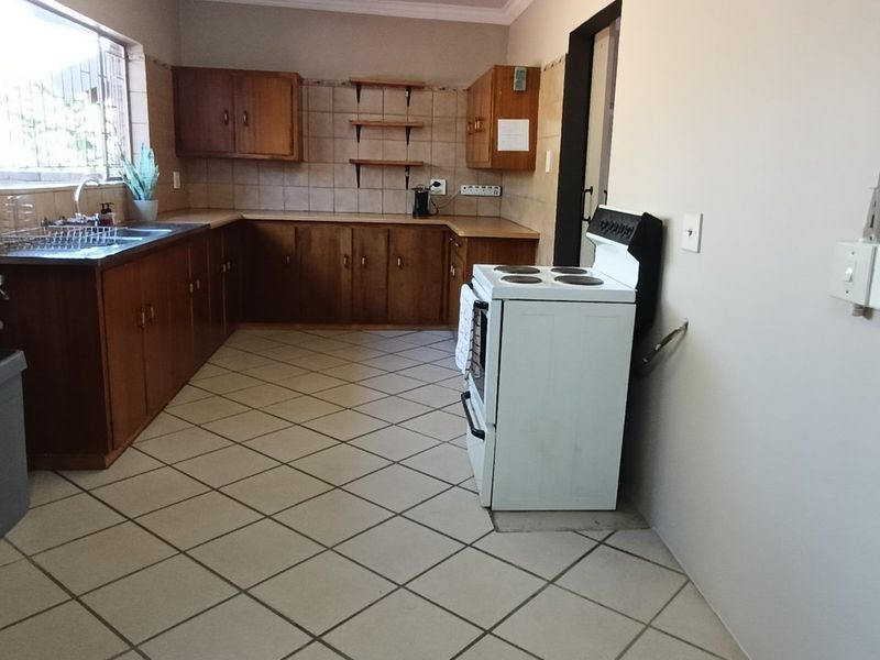 A functional kitchen featuring wooden cabinetry, tiled splashbacks, and ceramic flooring, offering a practical layout with potential for modern cosmetic updates.