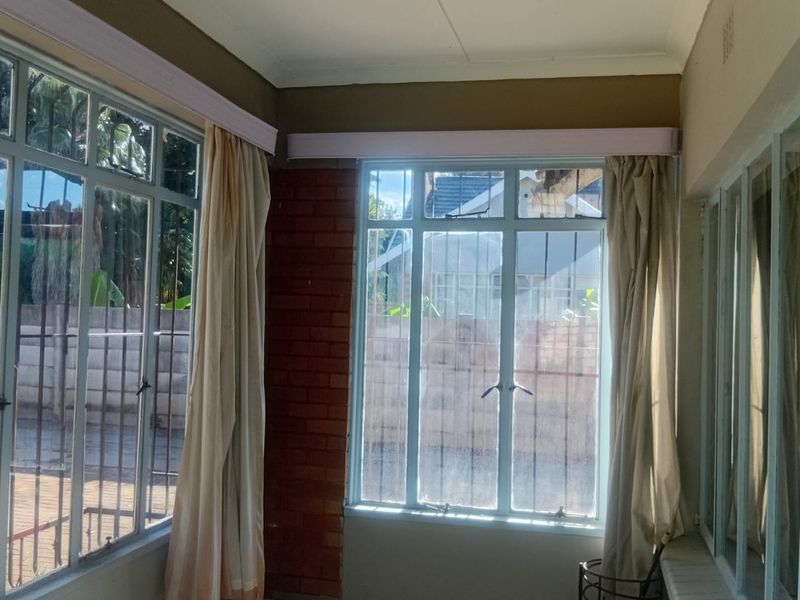 A sun-filled enclosed patio area featuring large steel-framed windows, exposed brick accents, and a coved ceiling, offering a bright space with garden views.