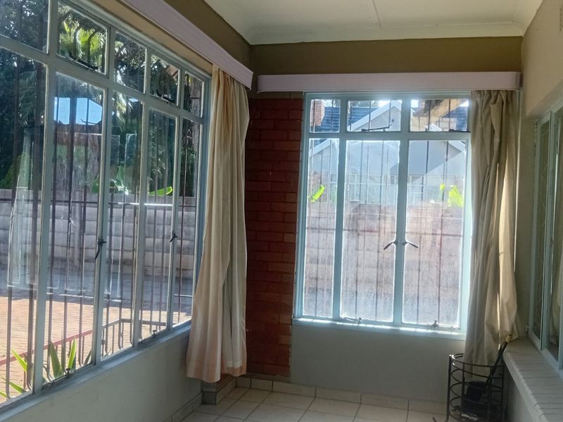 A sun-filled enclosed patio featuring large steel-framed windows, tiled flooring, and exposed brick accents, offering a bright and versatile space.