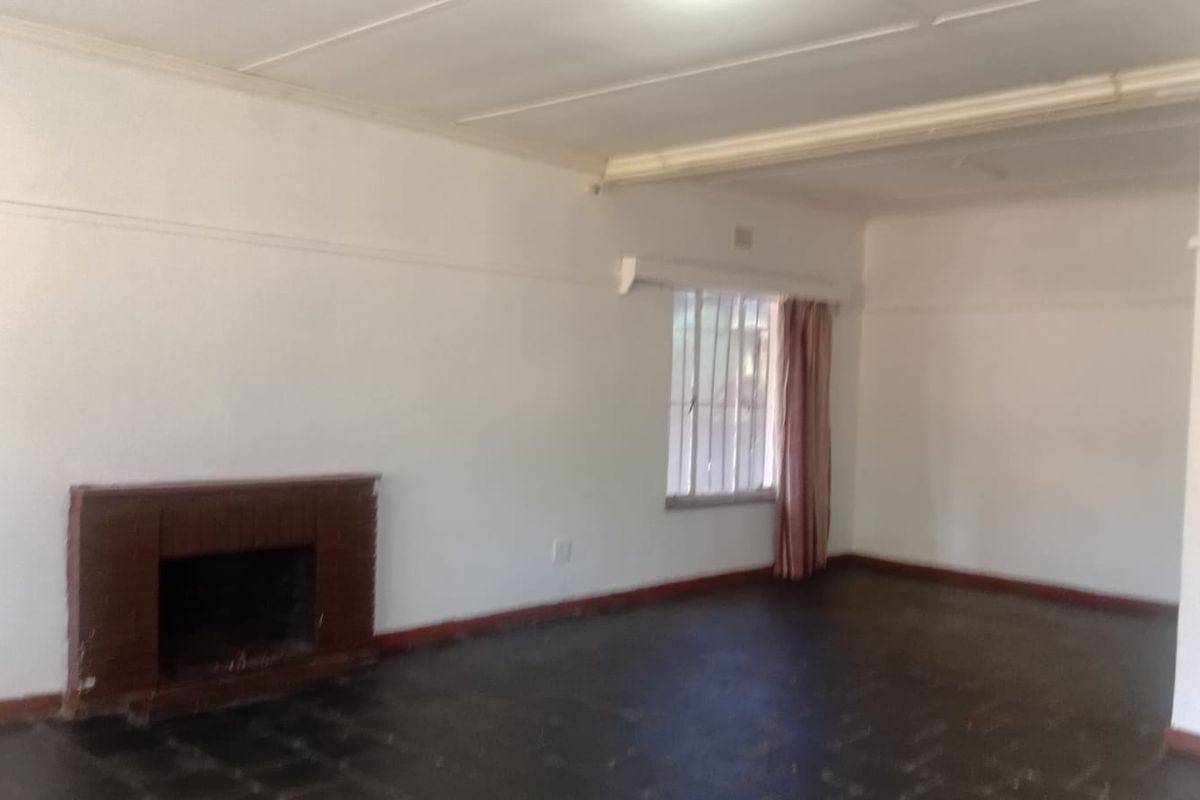An empty living room featuring a brick fireplace, dark flooring, and a window with security bars, offering a blank canvas for renovation.