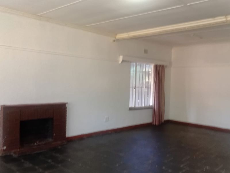 An empty living room featuring a brick fireplace, dark flooring, and a window with security bars, offering a blank canvas for renovation.