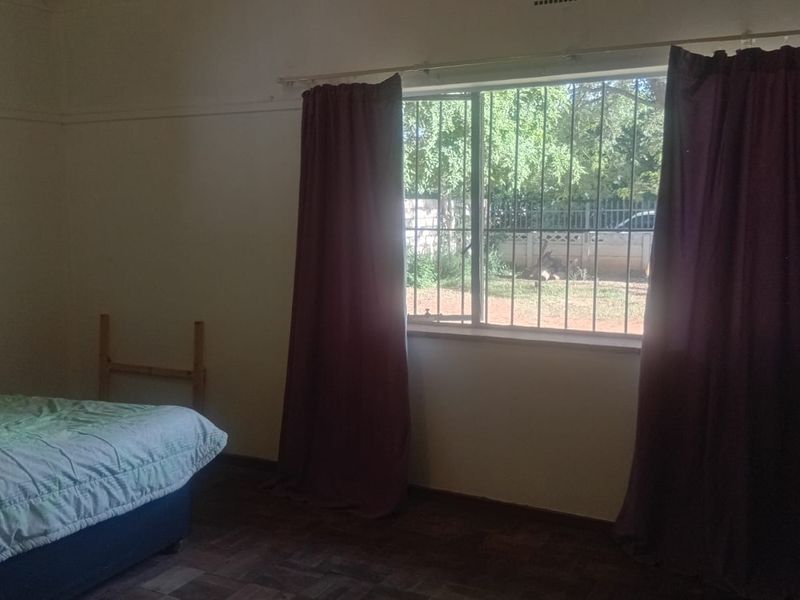 A bedroom featuring parquet flooring, a window with security bars, and a picture rail, offering a functional space with natural light.