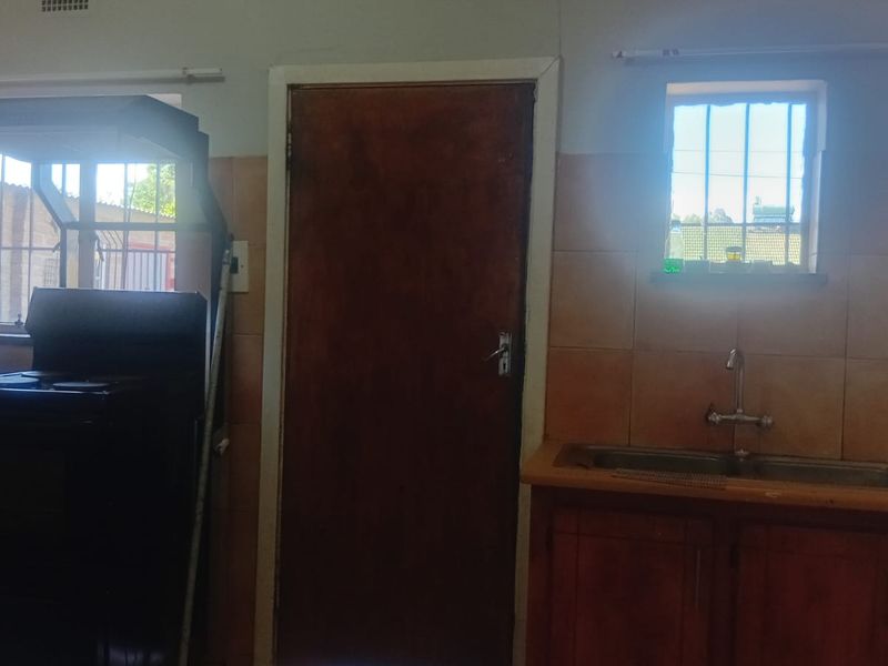 A functional kitchen featuring wooden cabinetry, a double bowl sink, tiled splashbacks, and security bars on the windows.