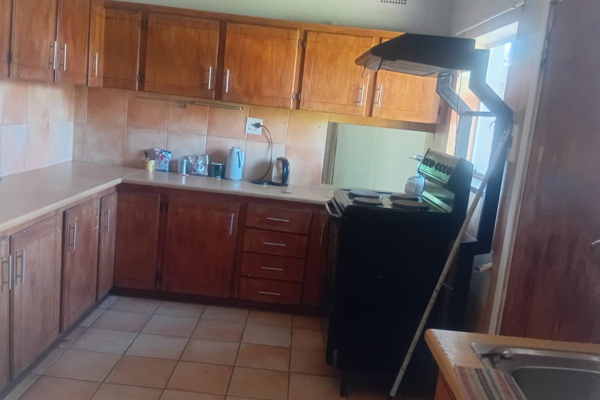 A dated kitchen featuring wooden cabinetry, tiled backsplash, and flooring, equipped with a freestanding stove and extractor fan.
