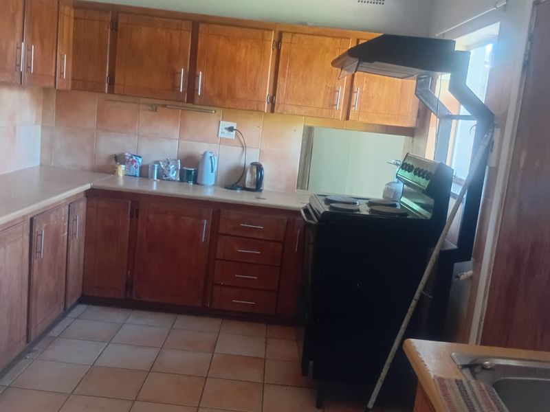 A dated kitchen featuring wooden cabinetry, tiled backsplash, and flooring, equipped with a freestanding stove and extractor fan.