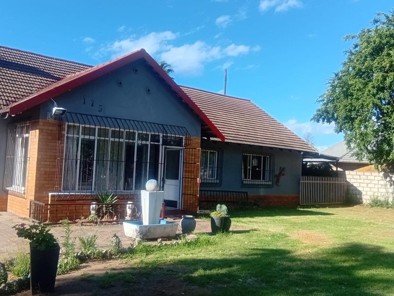 Front elevation of a single-story brick and plaster house featuring a tiled roof, paved driveway, and established garden area.