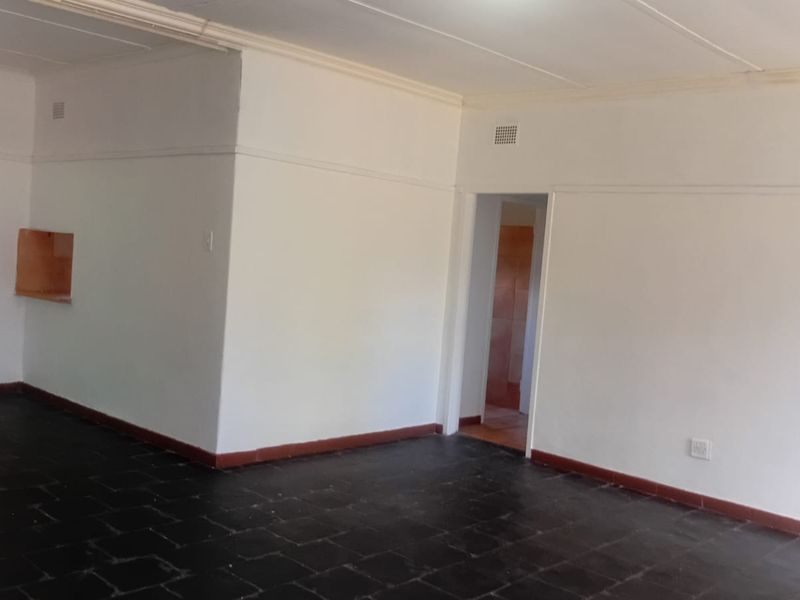 An empty living area featuring dark tiled flooring, white walls with cornice detailing, and a convenient wall pass-through to the adjacent space.