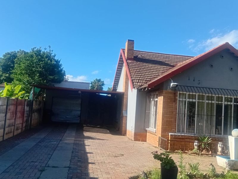 Front elevation of a single-story house featuring a brick driveway, attached carport, tiled roof, and security bars on windows.