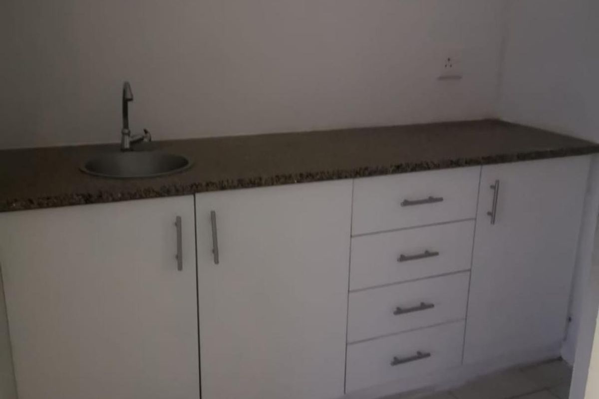 A functional scullery or kitchenette area featuring white built-in cabinetry, granite countertops, a stainless steel sink, and tiled flooring.