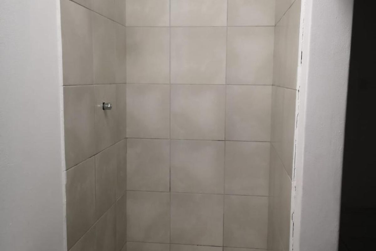 A compact bathroom featuring a tiled shower enclosure with a fixed shower head and a pedestal basin with a mixer tap.