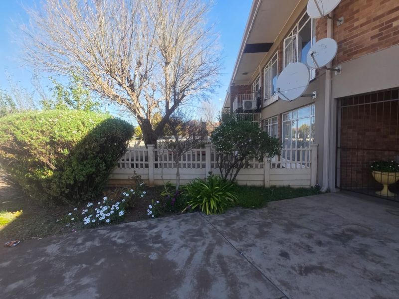Front exterior view of the apartment building featuring a brick facade, concrete driveway, and secure gated entrance with established garden landscaping.