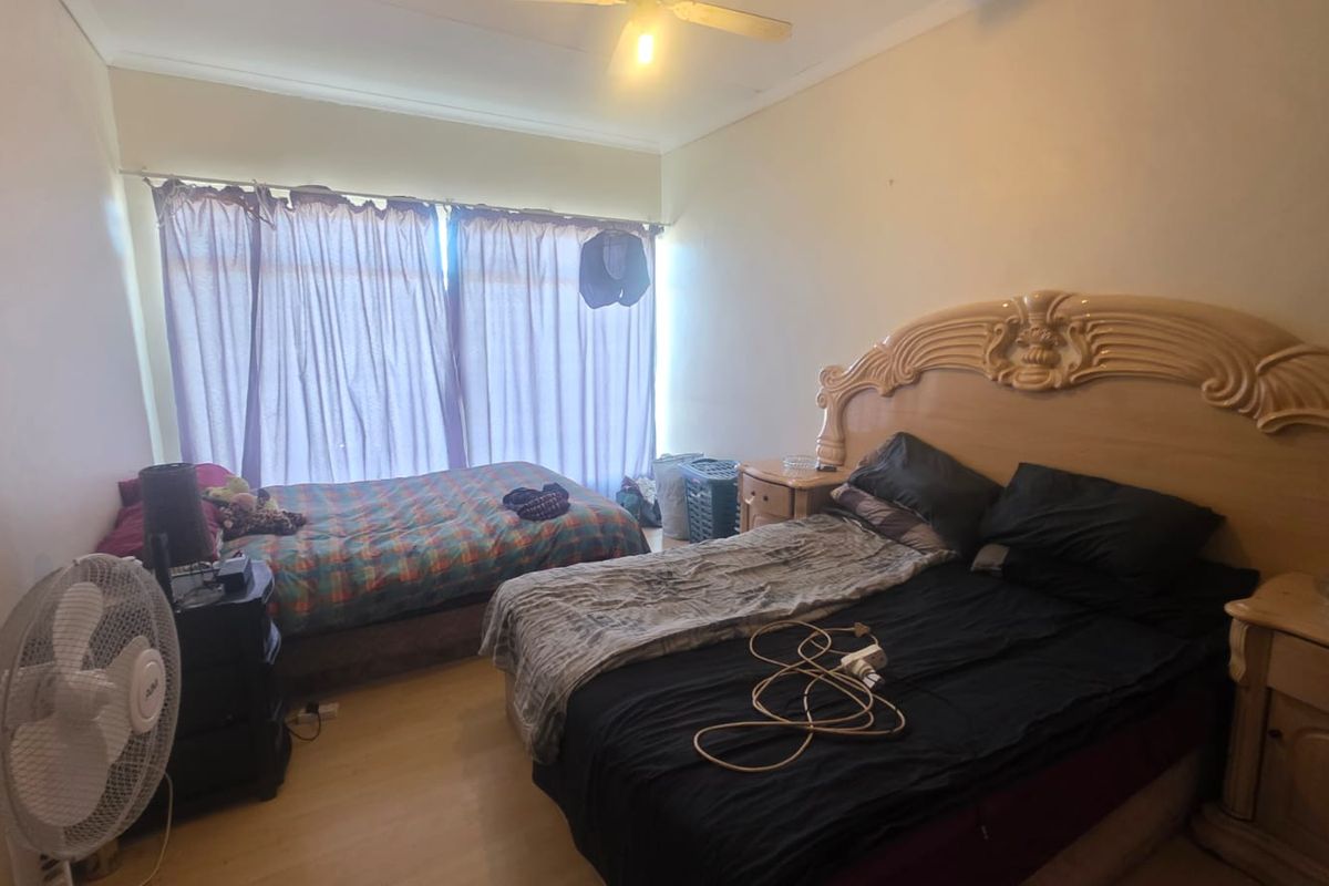 A bedroom featuring laminate flooring and a ceiling fan, offering a functional space with natural light through large window coverings.