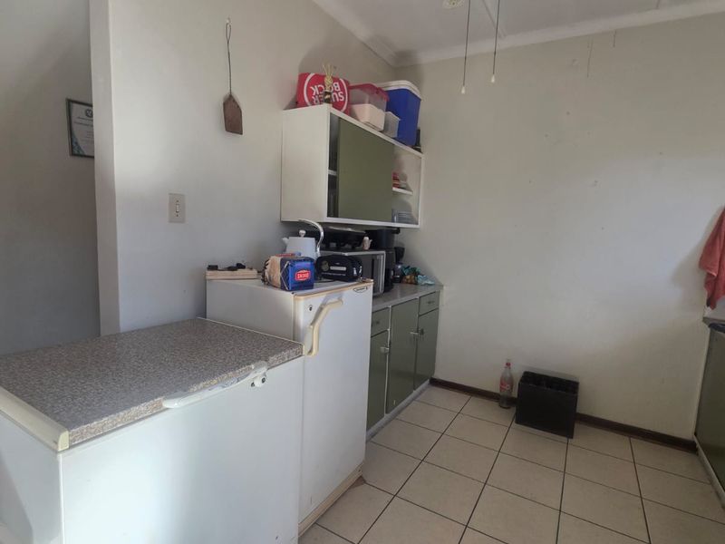 A functional kitchen area featuring built-in cabinetry, laminate countertops, and ceramic floor tiling, offering a practical layout with potential for cosmetic updates.