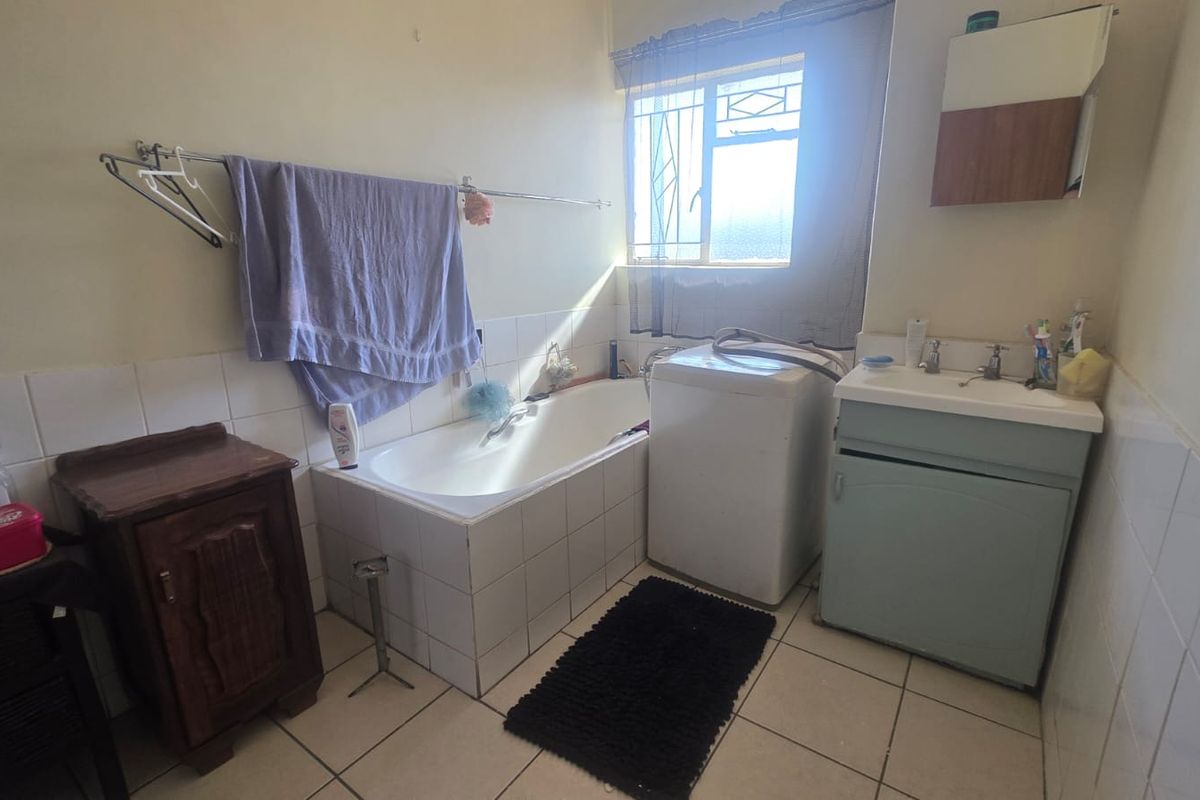 A functional bathroom featuring a built-in bathtub, tiled splashbacks, and a vanity basin, with ceramic floor tiles and security bars on the window.