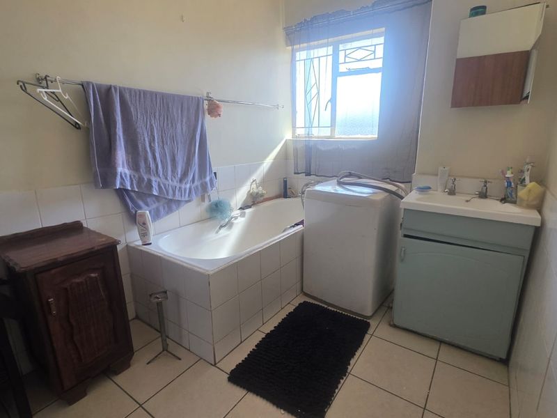 A functional bathroom featuring a built-in bathtub, tiled splashbacks, and a vanity basin, with ceramic floor tiles and security bars on the window.
