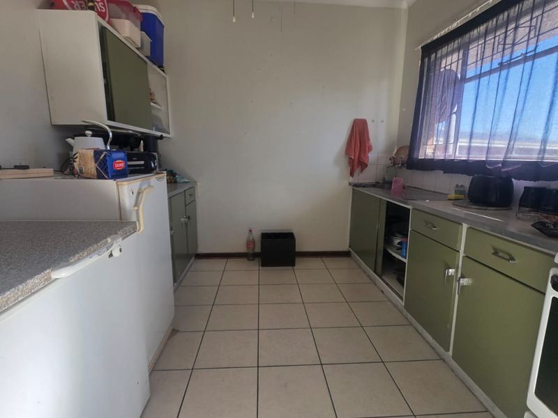 A dated kitchen featuring original cabinetry, tiled flooring, and a stainless steel sink, offering significant potential for modernization and renovation.