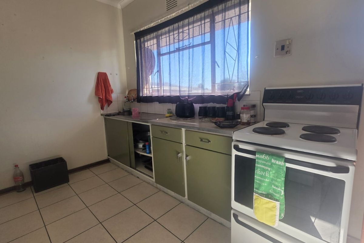A dated kitchen featuring original cabinetry, a stainless steel sink, tiled flooring, and a freestanding stove, offering potential for modernization and renovation.
