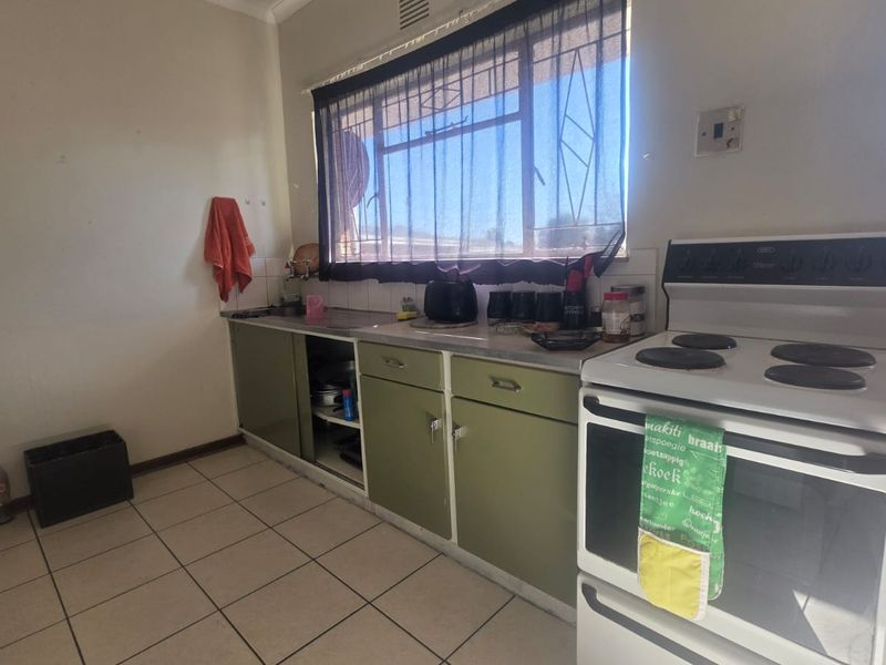 A dated kitchen featuring original cabinetry, a stainless steel sink, tiled flooring, and a freestanding stove, offering potential for modernization and renovation.