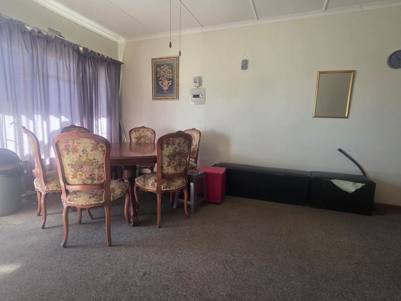 A dining area featuring carpet flooring and large windows with curtains, offering a functional space that would benefit from cosmetic updates.