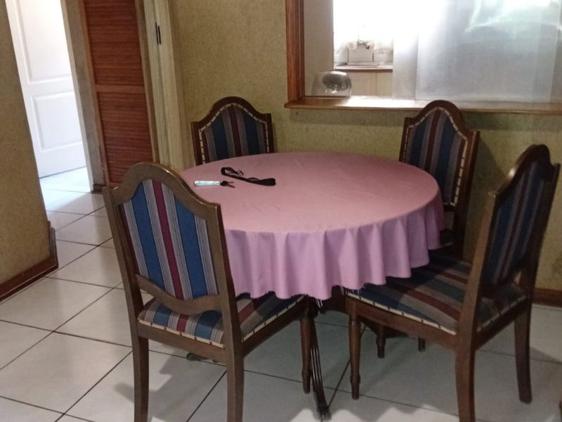 A dining area featuring tiled flooring and a serving hatch connecting to the kitchen, with dated wall finishes and traditional wooden door frames.